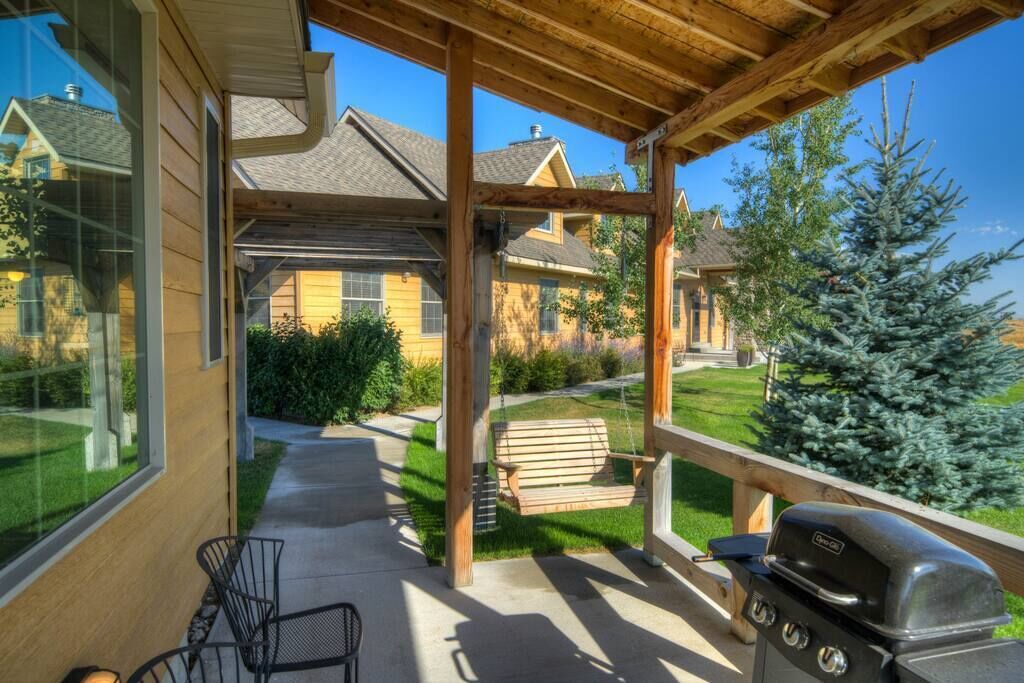 A covered patio with a grill, a swing, and a view of houses in the background.