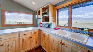 A kitchen with wooden cabinets, a sink, and a window with a mountain view. - 2-bedroom cabin with views of the Madison River! (Madison County)