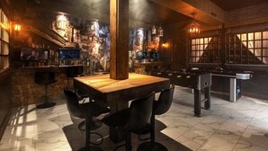 Zona de bar con una mesa de madera, sillas negras y barra.