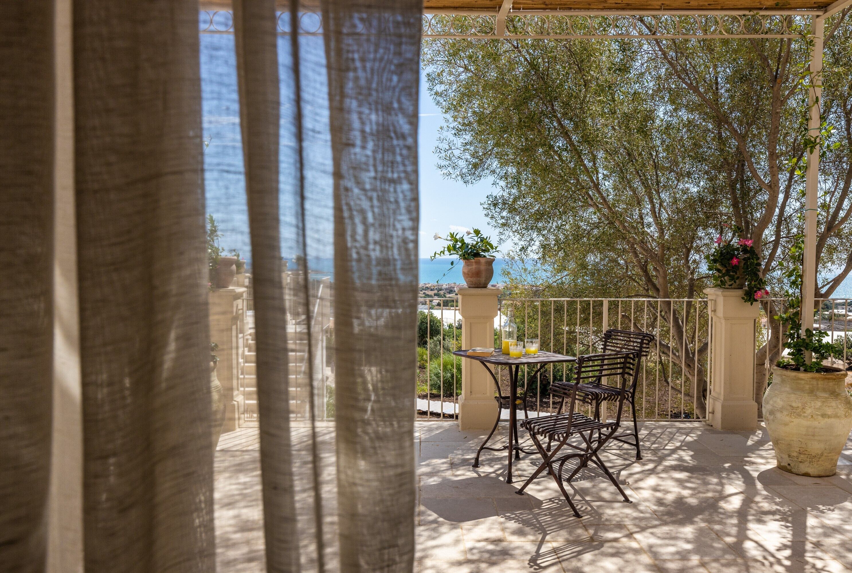Un patio exterior con una mesa y sillas, una planta en maceta y vista al mar.
