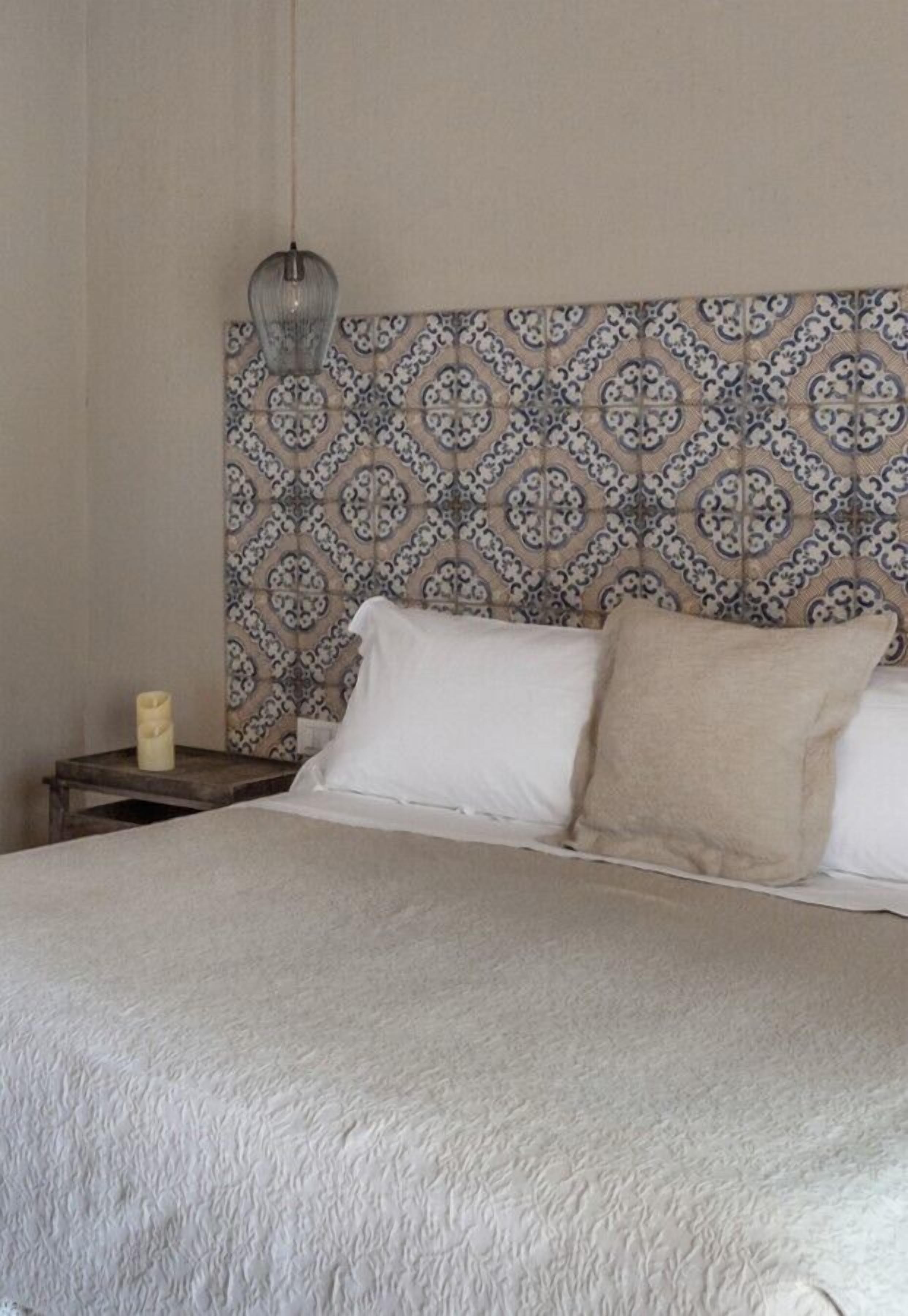 A bed with a patterned headboard, a bedside table with a candle, and a hanging light fixture.