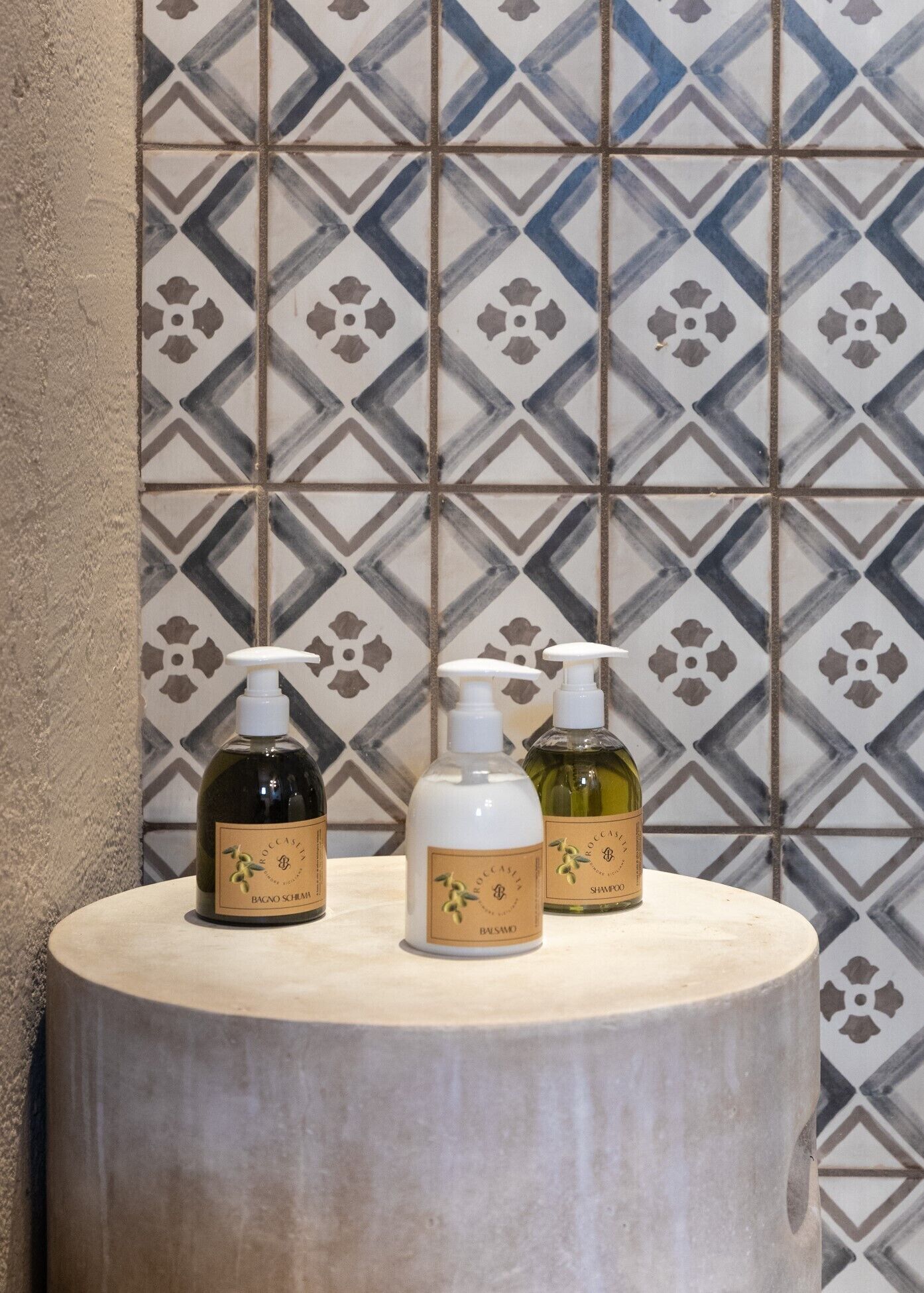 Three bottles of Roccasola Bagnomassimo on a round wooden table against a tiled wall.