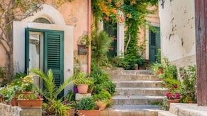 A narrow stone staircase leading up to a building with green shutters and a small porch area with potted plants. - RoccaSeta dimore siciliane (Scicli)