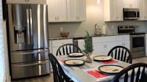 Une cuisine moderne dotée d’appareils électroménagers en acier inoxydable, de meubles blancs et d’une table à manger pour quatre personnes.