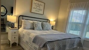 Une chambre à coucher avec un lit, des tables de chevet, un miroir et une fenêtre avec des stores.