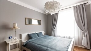 Quarto com cama, mesa de cabeceira, luminária, espelho e cortinas.