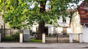Uma rua residencial com uma casa branca, uma árvore e um portão de metal.