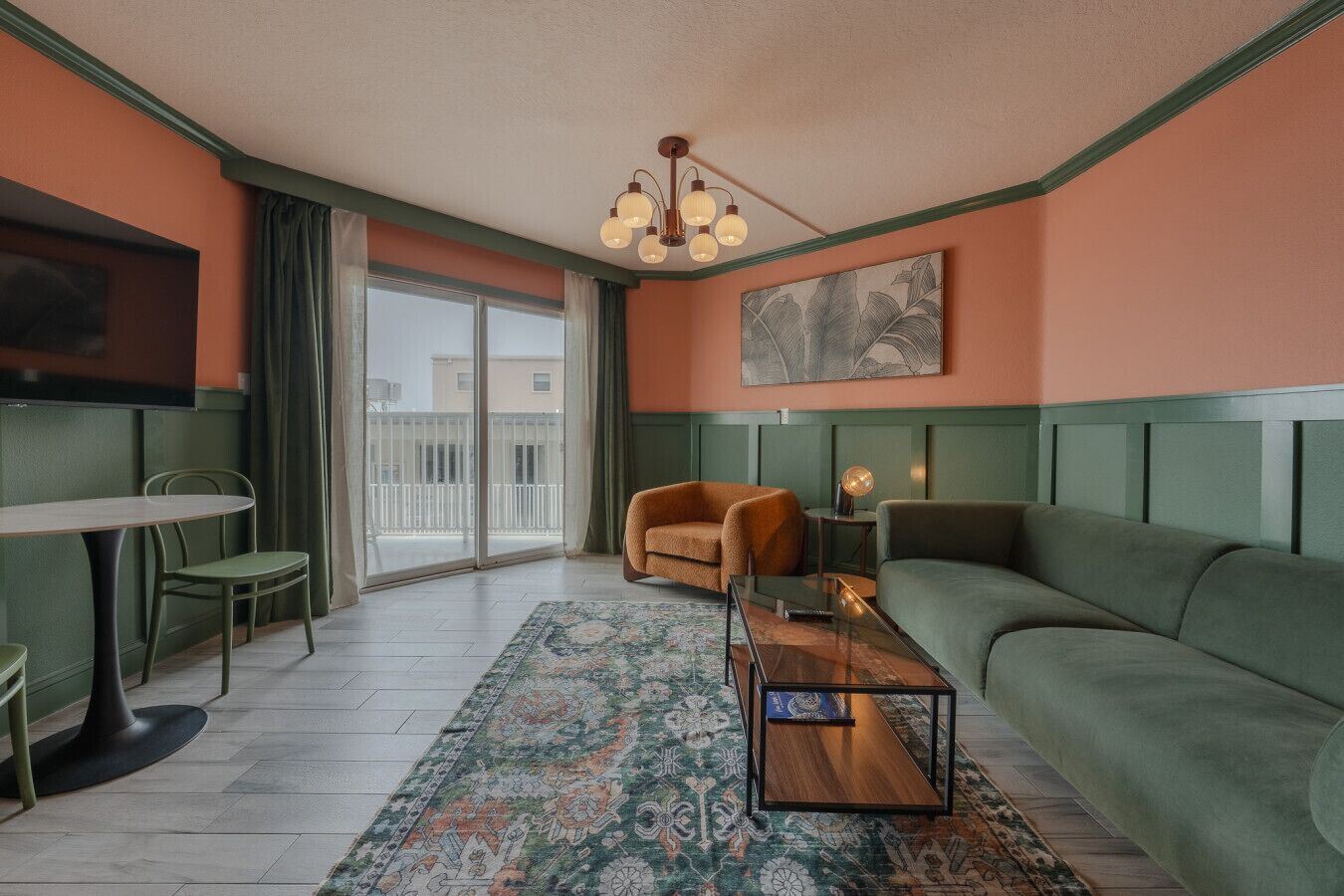 Una sala de estar moderna con un sofá verde, un sillón marrón, una mesa de centro de vidrio y una alfombra estampada.