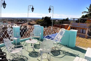 A rooftop terrace with white metal chairs and tables, a view of the city, and a fence. - Casa Vista  (Trinidad)