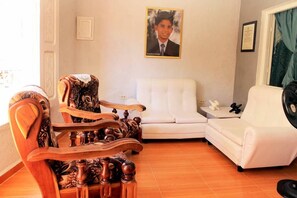 A living room with a white sofa, a wooden chair with intricate carvings, a framed photo on the wall, and a window with curtains. - Casa Vista  (Trinidad)