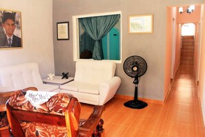 A living room with a white sofa, a wooden chair, a fan, and a framed certificate on the wall. - Casa Vista  (Trinidad)