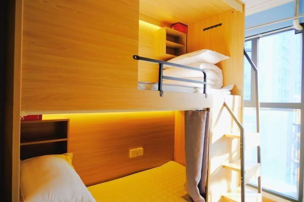 Ein kleines Zimmer mit Etagenbett, Schreibtisch und einem Fenster, das natürliches Licht hereinlässt.