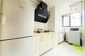 Una cocina con gabinetes blancos, una campana extractora negra, una ventana y un refrigerador.