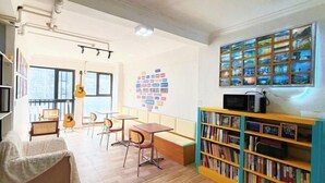 Ein Zimmer mit Bücherregal, Gitarre, Tisch und Stühlen.