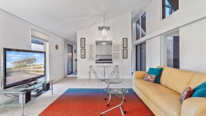 A modern living room with a TV, a glass coffee table, a sofa, and a colorful rug.
