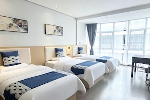 Habitación de hotel con dos camas, un escritorio y ventanas amplias.