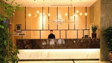 A hotel reception area with a marble counter, a receptionist, and a modern chandelier.