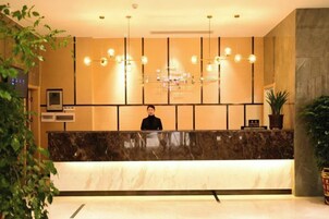 Zona de recepción de hotel con mostrador de mármol, una recepcionista y una lámpara de araña moderna.