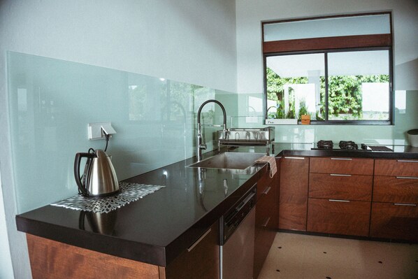 A modern kitchen with a stainless steel kettle, a sink, and wooden cabinets.