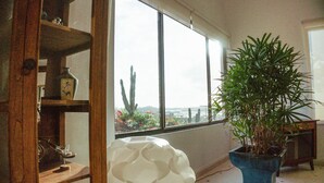 Een kamer met een groot raam, een kamerplant en een houten plank met diverse voorwerpen.