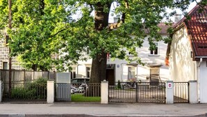 Ein von einer Mauer umschlossenes Wohngebiet mit einem großen Baum, einem weißen Gebäude mit rotem Dach und einem abgestellten Motorrad.
