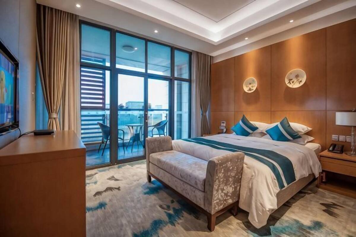 Een hotelkamer met een groot bed, een bureau, een stoel, een balkon met uitzicht en een groot raam.