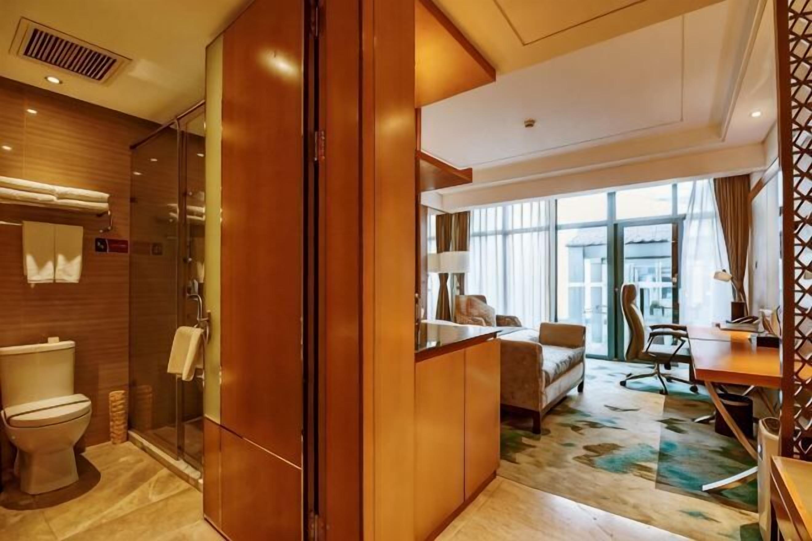 A hotel room with a shower, toilet, bed, desk, and a view of the city.
