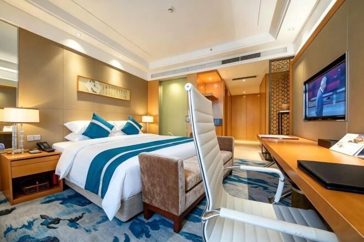 Een hotelkamer met een bed, nachtkastjes, een bureau, een stoel, een televisie en een tv aan de muur.