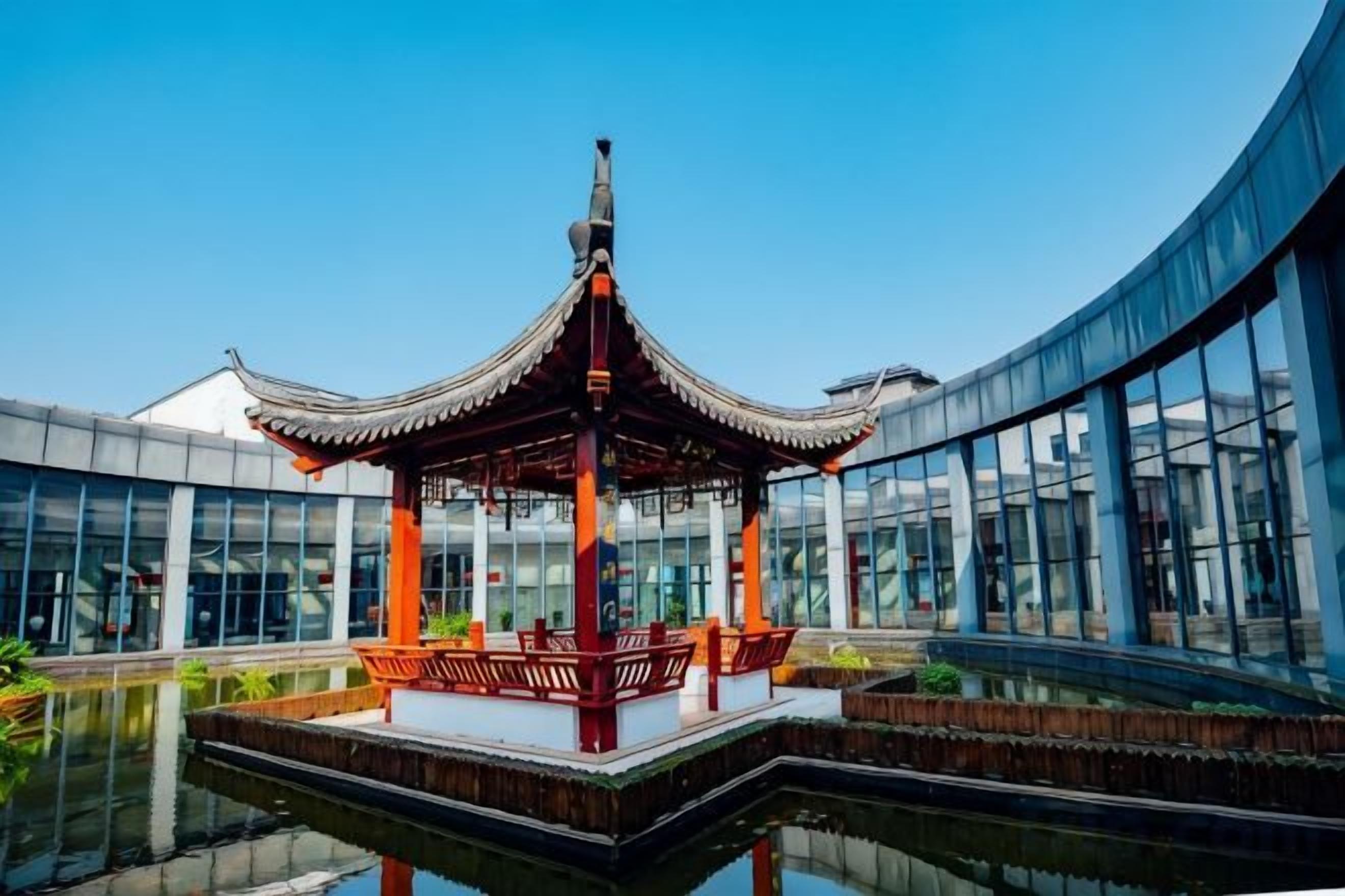 Een klassiek paviljoen met pannendak, omgeven door een vijver, voor een modern gebouw met grote glasramen.
