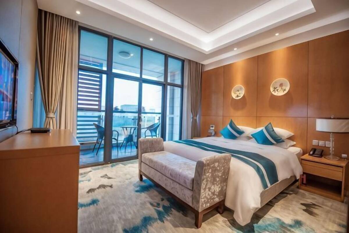 Een hotelkamer met een groot bed, een bureau, een stoel, een televisie en een balkon met uitzicht.