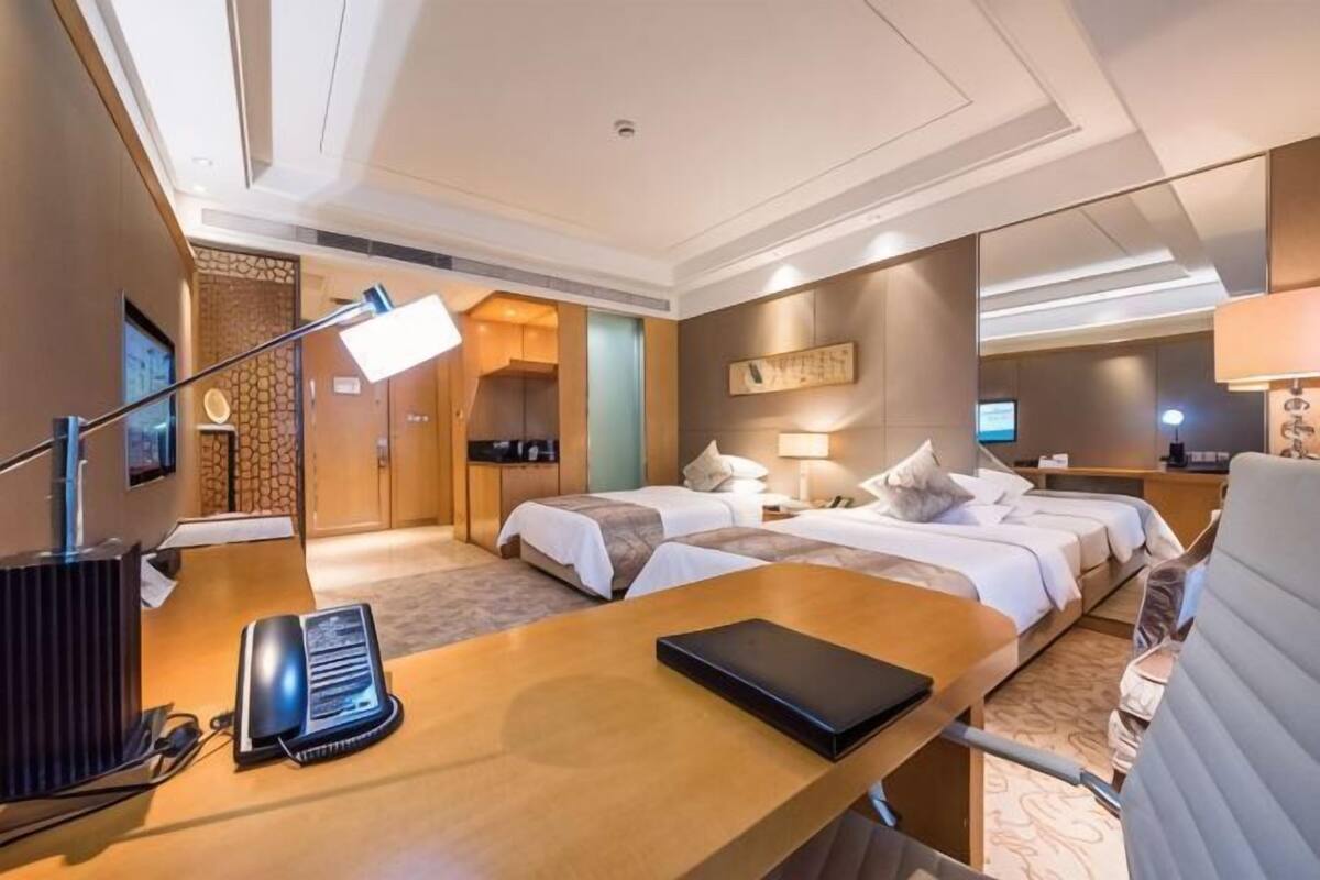 Een hotelkamer met twee bedden, een bureau met een lamp, een telefoon en een televisie.