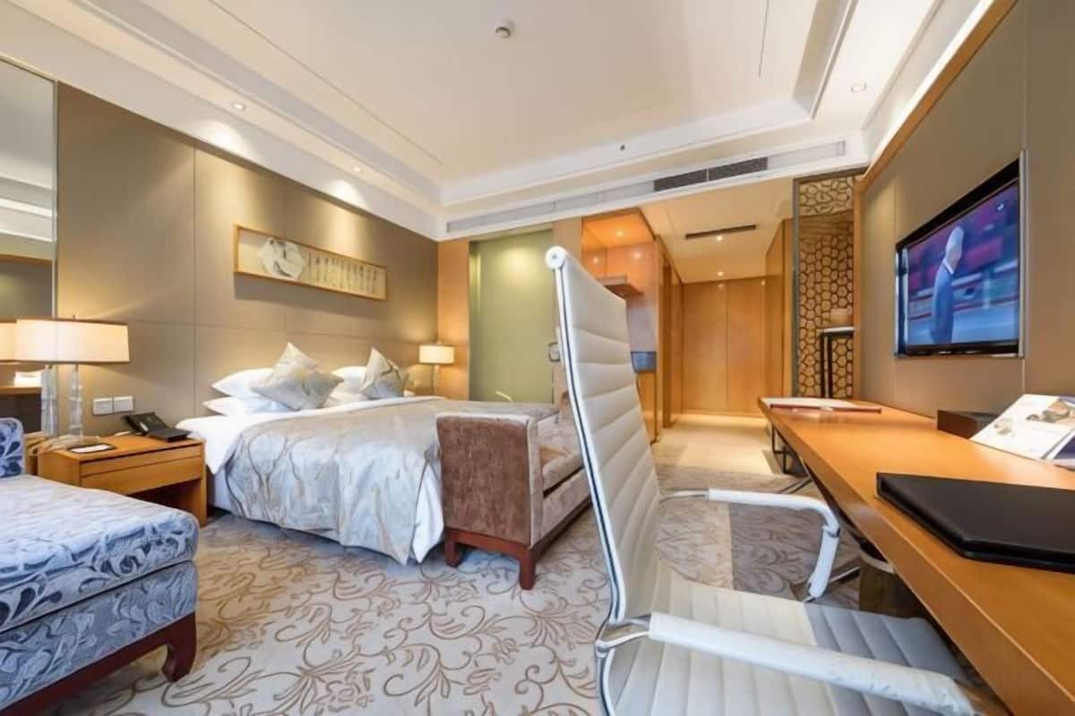 A hotel room with a bed, bedside table, chair, desk, TV, and a large mirror.