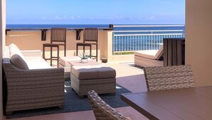 A sunlit outdoor seating area with wicker furniture and a view of the ocean.