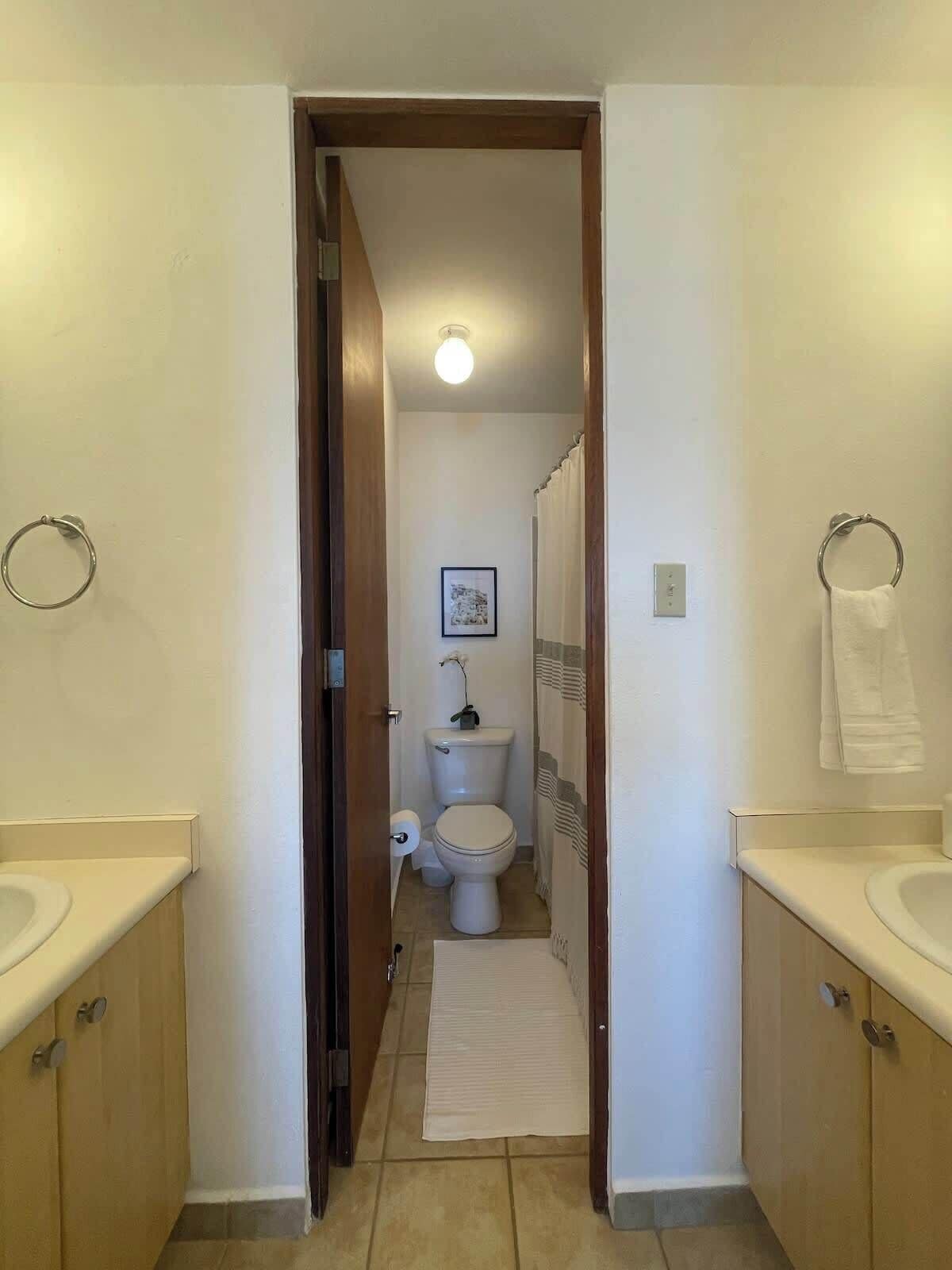 Ein schmaler Flur, der zu einem Badezimmer mit Toilette, Waschbecken und Handtuchhalter führt.