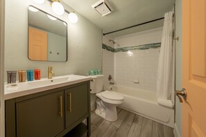 Ein Badezimmer mit einem weißen Waschbecken, Spiegel und Toilette. Ein Duschvorhang und ein Handtuch hängen an der Wand.