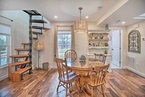 A dining area with a round glass table and wooden chairs, a spiral staircase, and a hanging light fixture.