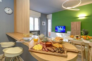 A breakfast setup with eggs, bacon, sausages, mushrooms, toast, and orange juice on a wooden board.