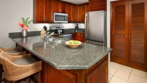 A kitchen with granite countertops, wooden cabinets, stainless steel appliances, and wicker bar stools.