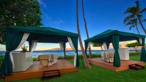 Two outdoor tents with white furniture, set on a grassy area with a view of the ocean.