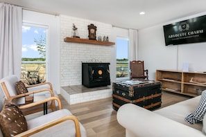 A living room with a fireplace, a television, a suitcase, and a view of the outdoors. - 4/2 Ranch | Hot Tub | Full Kitchen | Family Friendly (Fredericksburg)