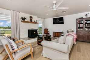 Ein modernes Wohnzimmer mit einem weißen Sofa, Holzsesseln, einem Kamin, einem Fernseher und einem Bücherregal.