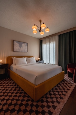 Een hotelkamer met een groot bed, een nachtkastje, een rode stoel, een schilderij aan de muur en een kroonluchter.