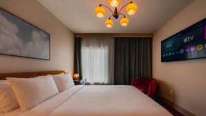 Una camera d'albergo con un letto grande, una TV a parete e una finestra con tende.