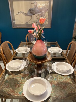 A dining table set with white plates, glasses, and a vase with pink flowers.
