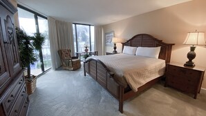 A hotel bedroom with a large bed, a chair, a nightstand, a lamp, and a view of the outdoors through a window. - Best Ocean View-Overlooks Splash Pad-1st Floor-Edgewater 1-110! Beachfront Master-2 BD/2BTH! (Panama City Beach)