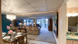 A spacious living area with a large window, a dining table set for four, and a kitchen area visible in the background. - Best Ocean View-Overlooks Splash Pad-1st Floor-Edgewater 1-110! Beachfront Master-2 BD/2BTH! (Panama City Beach)