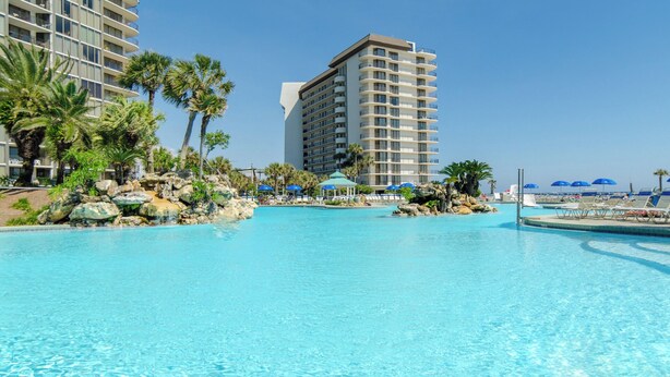 A large, clear swimming pool with a rock formation and palm trees, surrounded by hotel buildings. - Best Ocean View-Overlooks Splash Pad-1st Floor-Edgewater 1-110! Beachfront Master-2 BD/2BTH! (Panama City Beach)