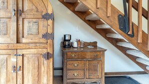 Uma escada de madeira com corrimão, um armário de madeira com gavetas e uma cafeteira sobre o armário.