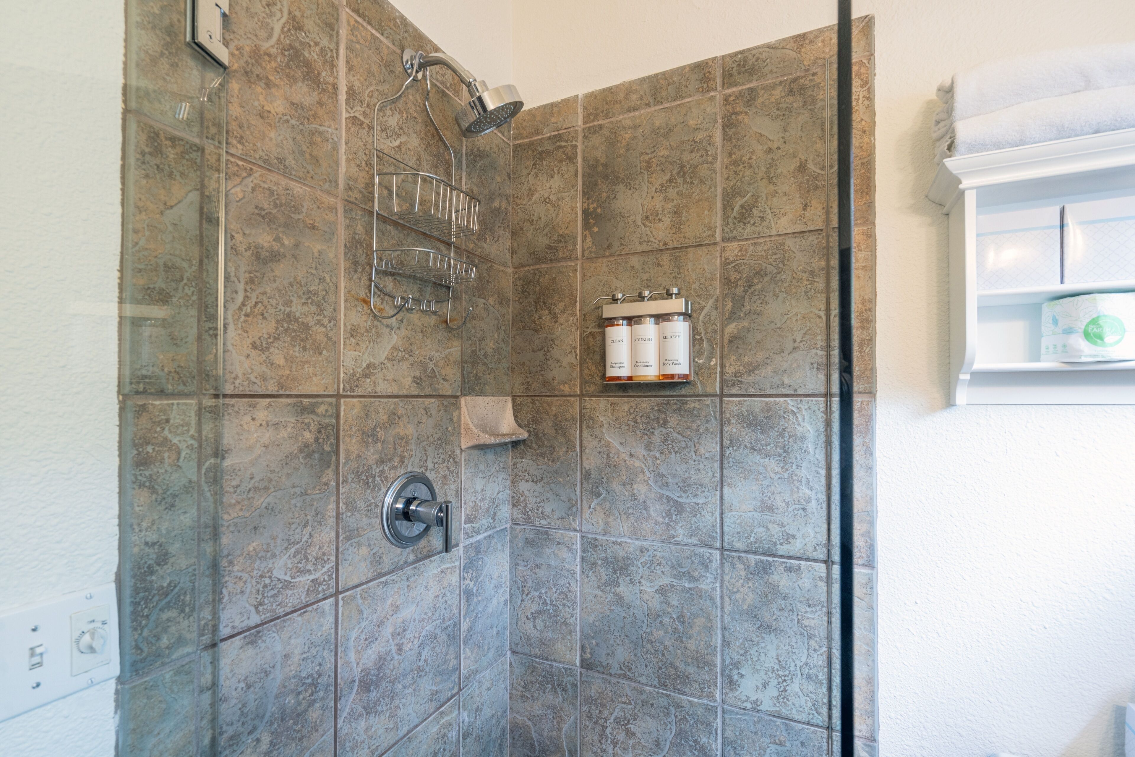 Una ducha con puerta de cristal, cabezal de ducha metálico y estante con artículos de aseo.