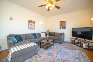A living room with a grey sectional sofa, a coffee table, a flat-screen TV, and a patterned rug.